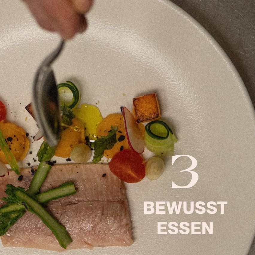 Ein Teller mit einem Stück Lachs, garniert mit Gurke und Spargel, und verschiedenen Gemüsesorten. Eine Hand hält eine Gabel, bereit zum Essen. Der Teller hat die Nummer 3 und den Text 'BEWUSST ESSEN'.