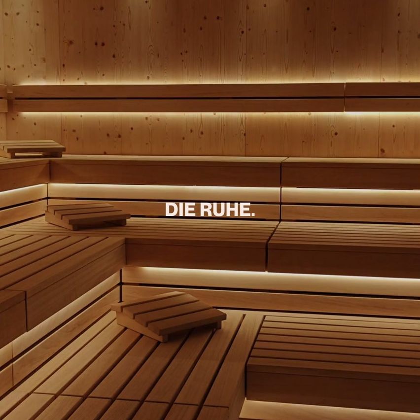 Ein holzverkleideter Saunaraum mit Bänken und einer warmen, einladenden Atmosphäre. Der Text 'DIE RUHE' ist prominent angebracht.