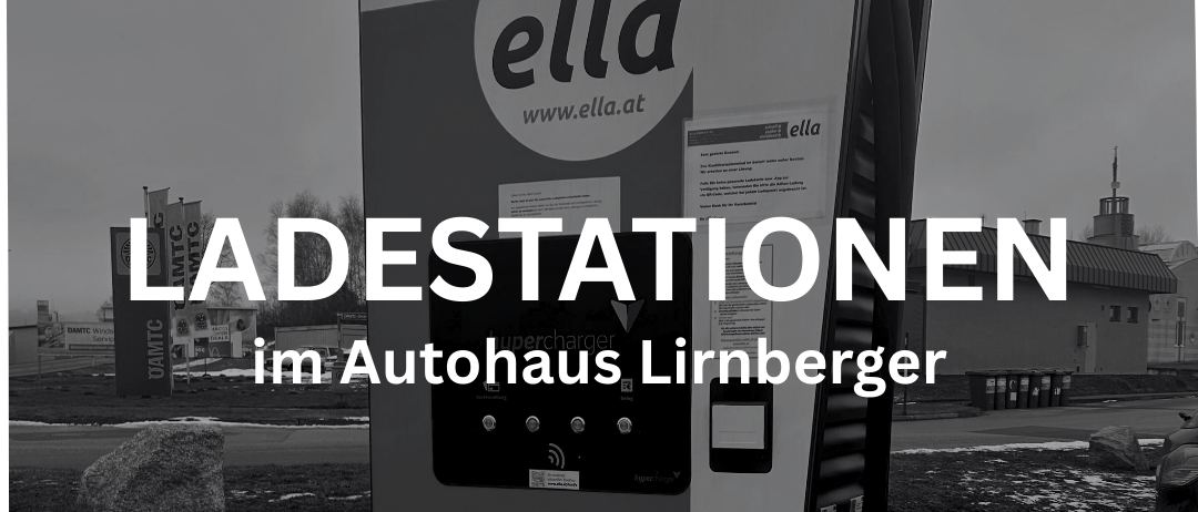 Ein Schwarz-Weiß-Foto zeigt eine Elektroauto-Ladestation mit 'ella'-Marke. Sie ist vor einem verschwommenen Hintergrund mit einem Gebäude und Bäumen zu sehen. Die Station zeigt 'LADESTATIONEN' und 'im Autohaus Lirnberger' Text.