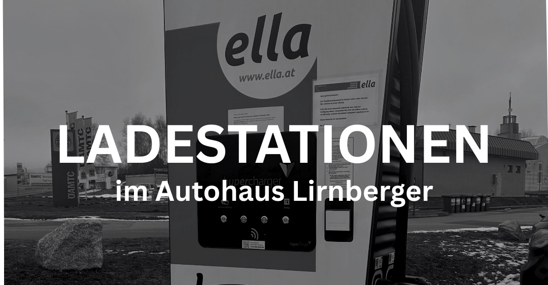 Ein Schwarz-Weiß-Foto zeigt eine Elektroauto-Ladestation mit 'ella'-Marke. Sie ist vor einem verschwommenen Hintergrund mit einem Gebäude und Bäumen zu sehen. Die Station zeigt 'LADESTATIONEN' und 'im Autohaus Lirnberger' Text.