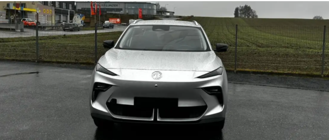 Ein glänzendes silbernes Auto ist auf einem nassen Parkplatz geparkt, mit einem Gebäude und Bäumen im Hintergrund.