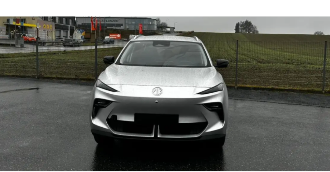 Ein glänzendes silbernes Auto ist auf einem nassen Parkplatz geparkt, mit einem Gebäude und Bäumen im Hintergrund.