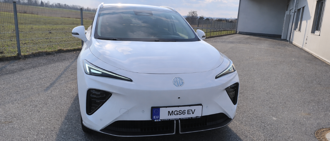 Ein weißer MGS6 EV ist vor einem Gebäude mit Zaun geparkt.