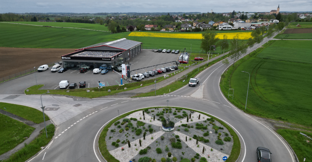 Eine Luftaufnahme eines Autohauses mit mehreren geparkten Autos auf dem Parkplatz und einem Kreisverkehr im Vordergrund.