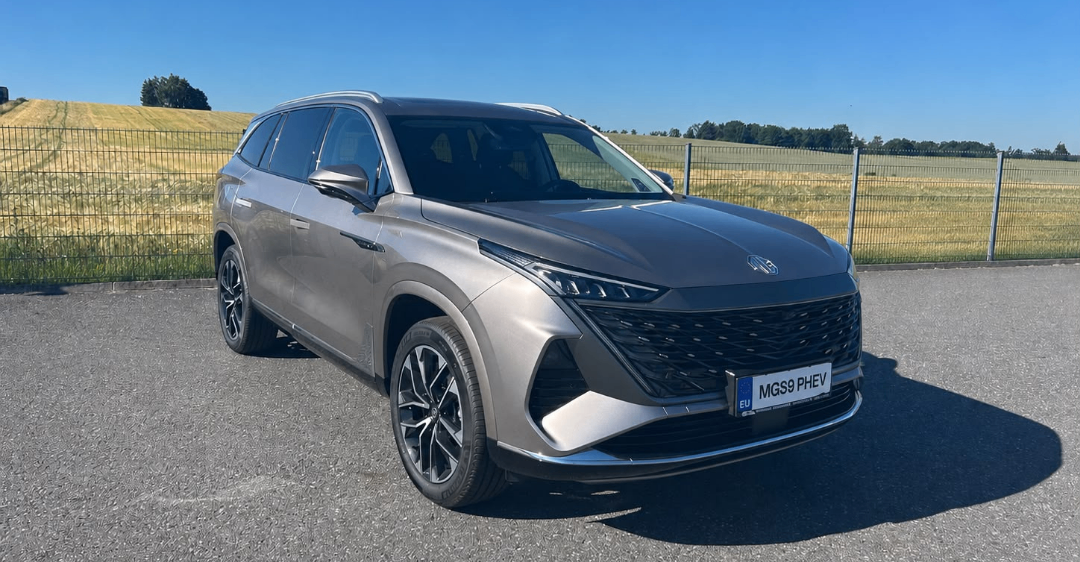 Ein grauer Toyota Highlander SUV mit dem Kennzeichen MGS9 PHEV vor einem Zaun geparkt.