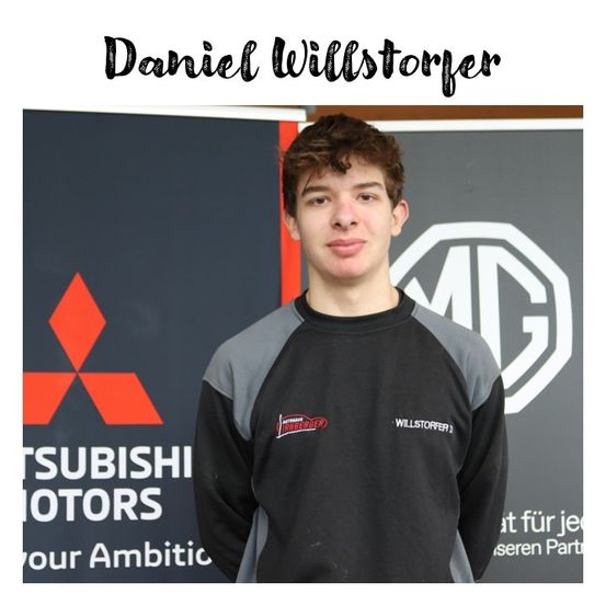 Daniel Willstorfer steht vor einem Mitsubishi Motors-Banner. Er trägt ein schwarzes und graues Langarmshirt mit Mitsubishi- und MG-Logos.
