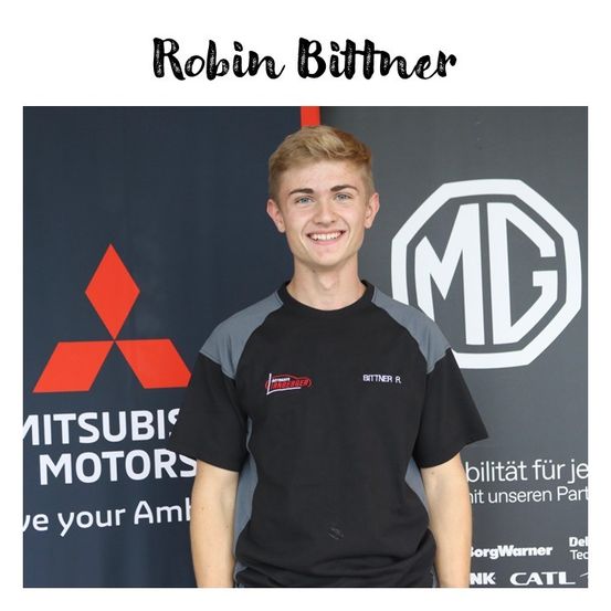 Ein junger Mann steht vor einer Kulisse mit Mitsubishi Motors und MG Logos. Er trägt ein schwarzes und graues Shirt mit einem roten Logo. Er lächelt und blickt nach vorne.