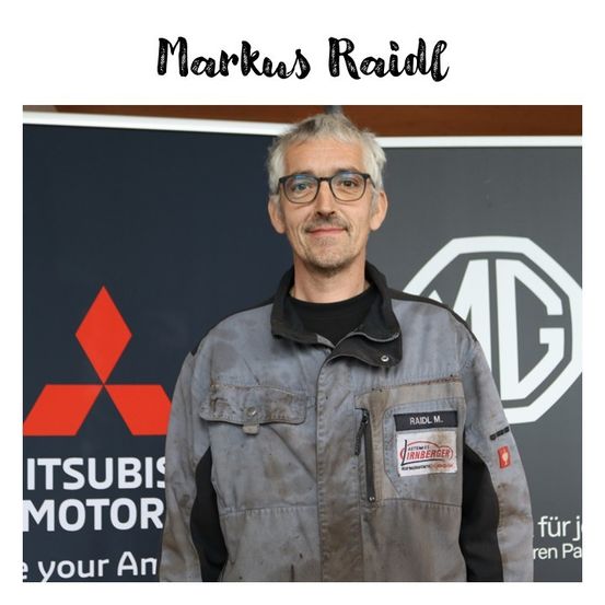 Ein Mann steht vor einem Mitsubishi-Motor-Schild. Er trägt eine graue Jacke und eine Brille. Die Jacke hat einen Aufnäher mit der Aufschrift 'Raidl M.'. Der Hintergrund ist dunkel mit Mitsubishi- und MG-Logos.
