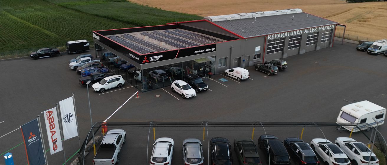 Ein Luftbild einer Autowerkstatt mit vielen geparkten Autos. Das Gebäude hat eine Solaranlage auf dem Dach.