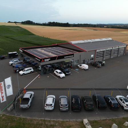 Eine Luftaufnahme einer Mitsubishi Motors-Vertretung mit Solardach und mehreren geparkten Autos auf dem Parkplatz.