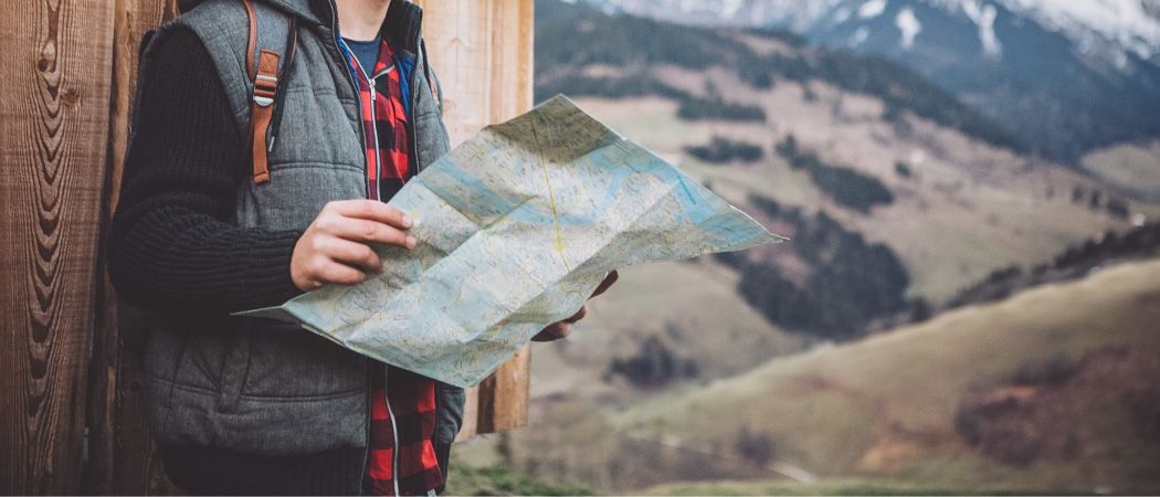Eine Person, die eine Karte in einem Gebirgsgebiet hält, trägt einen Rucksack und eine Weste.