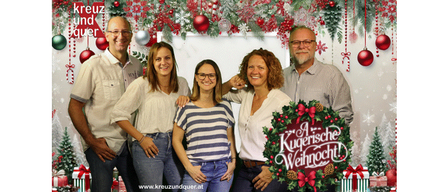 Eine Familie mit fünf Personen steht vor einem festlichen Weihnachtshintergrund. Zwei Männer und drei Frauen, lächelnd und posierend für ein Foto.