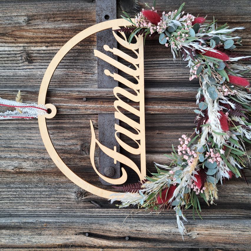 A wooden wreath with the word Family written in cursive and decorated with various colored flowers and leaves.