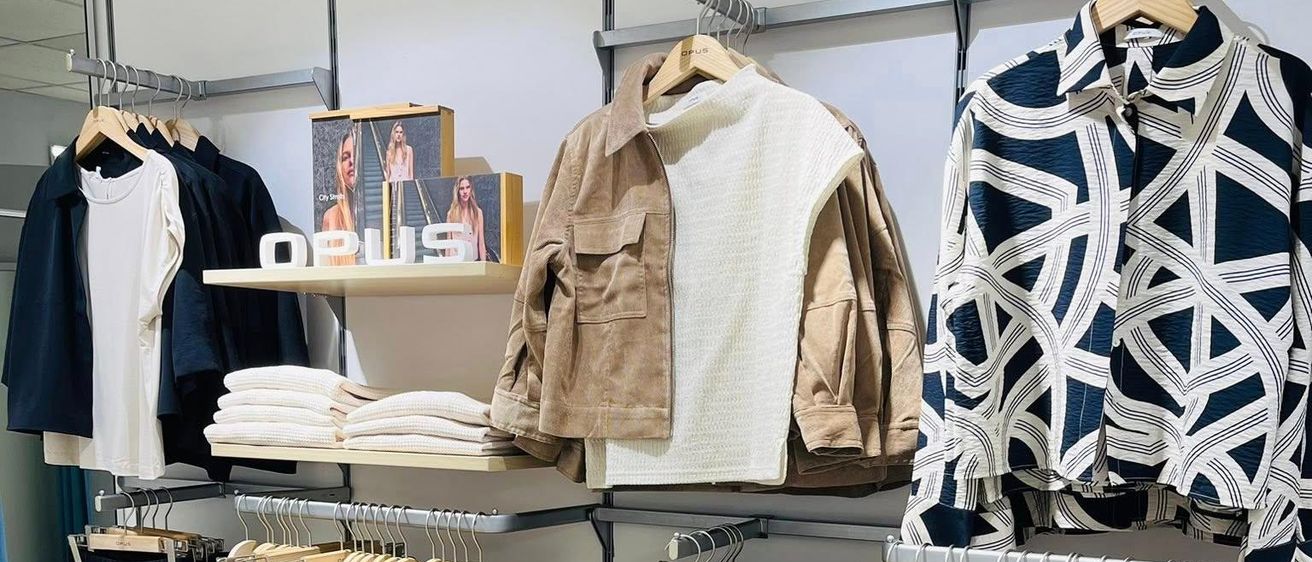 Ein Bekleidungsgeschäft mit einer Vielzahl von Kleidern an Kleiderbügeln und Regalen. Es gibt verschiedene Farben und Stile von Kleidung.