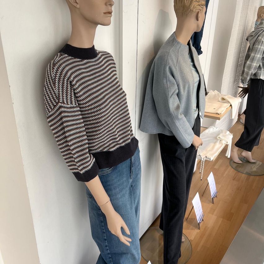 Zwei Mannequins stehen in einem Bekleidungsgeschäft, eines trägt einen schwarz-weiß gestreiften Pullover und Jeans, das andere eine graue Jacke und schwarze Hose.