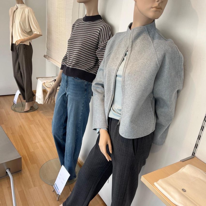 Drei Mannequins in einem Bekleidungsgeschäft zeigen verschiedene Outfits. Das linke Mannequin trägt ein beigefarbenes Oberteil und Hose, das mittlere ein gestreiftes Sweatshirt und Jeans, und das rechte ein graues Jackett und Hose.