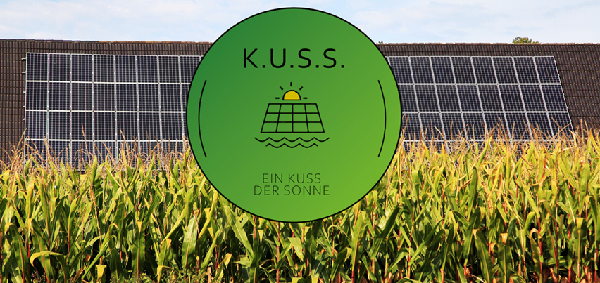 Ein grüner kreisförmiger Logo mit dem Text 'K.U.S.S.' ist vor einer Solarpanel-Anlage inmitten eines Maisfelds zu sehen.