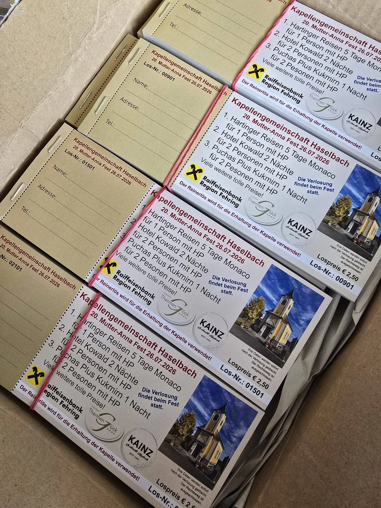 Eine Box mit mehreren Broschüren für Mutter-Anna-Fest 2026 in Haselbach. Die Broschüren enthalten Details über die Veranstaltungsdaten, Preise und die Raiffeisenbank Region Thermen.