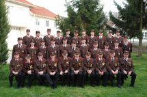 Eine Gruppe uniformierter Personen, möglicherweise Militärangehörige, posiert für ein Foto auf einem Rasen vor einem Gebäude.
