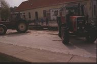 Ein roter Traktor ist neben einem Gebäude in Renovierung geparkt. Einige Leute stehen davor, einer von ihnen hält ein Werkzeug.