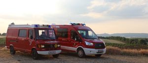 Zwei rote Krankenwagen sind auf einem Feldweg unter einem bewölkten Himmel geparkt. Einer ist mit 'Feuerwehr' und der andere mit 'Herrnwehr' beschriftet.
