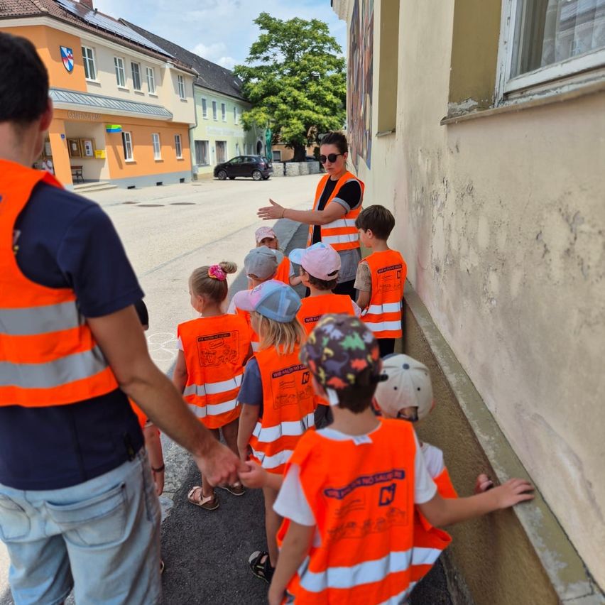 Kindergartenkinder in orange Warnwesten mit Betreuerin auf einem Gehsteig in Österreich