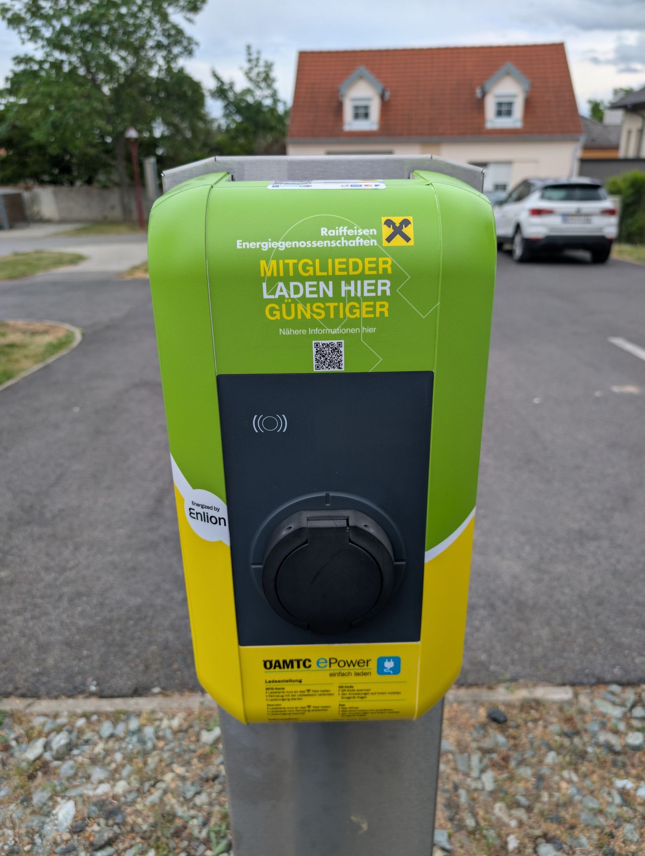 Eine grüne Ladestation am Straßenrand mit einem Hinweisschild für Mitglieder. Es gibt einen QR-Code für weitere Informationen.