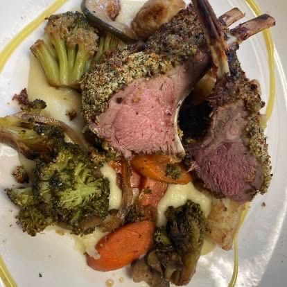 Ein Teller mit Lammkarree mit knuspriger Kruste, begleitet von Kartoffelpüree, Brokkoli, Karotten und Pilzen. Das Lamm hat eine zarte und saftige Textur.