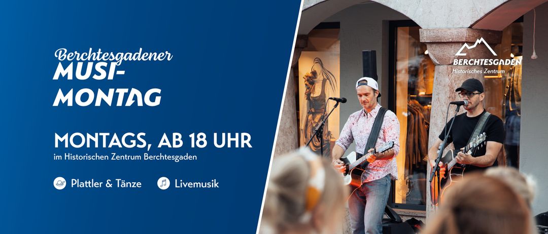 Ein Mann spielt Gitarre vor einem Gebäude. Es gibt ein Mikrofon und einen Musiklautsprecher auf einem Ständer.
