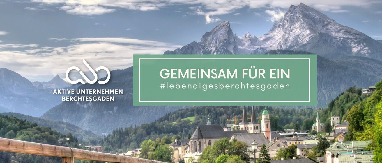 Ein landschaftliches Bild zeigt eine Bergregion mit einer Stadt darunter, präsentiert einen klaren Himmel mit Wolken. Im Vordergrund befindet sich ein Holzzaun. Der Text lautet 'GEMEINSAM FÜR EIN LEBENDIGES BERICHTESGADEN'.