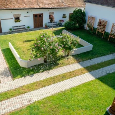 Ein Luftbild eines weißen Gebäudes mit braunem Dach, einem Garten und einem Ziegelweg.