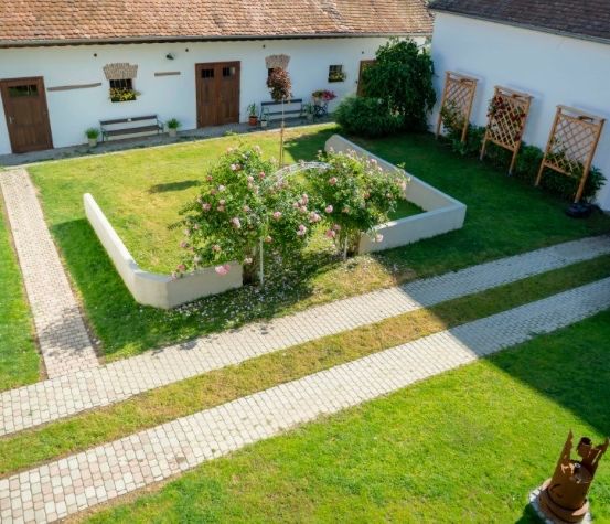 Ein Luftbild eines weißen Gebäudes mit braunem Dach, einem Garten und einem Ziegelweg.