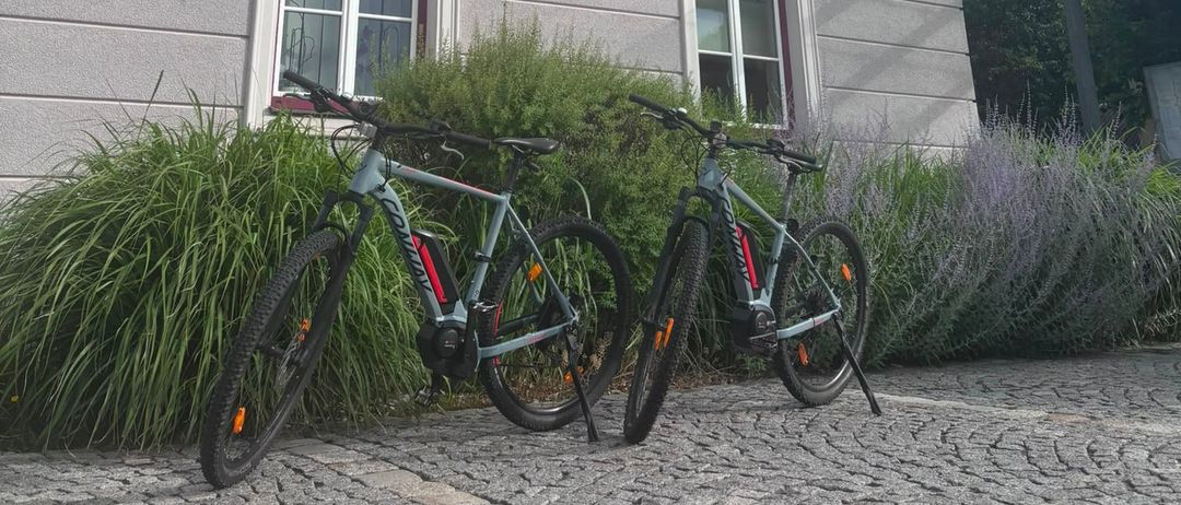 Zwei Fahrräder sind vor einem Gebäude namens Gemeindeamt geparkt, mit Pflanzen und blauem Himmel.