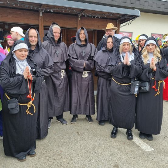 Eine Gruppe von Menschen in Mönchs- und Nonnenkostümen posiert für ein Foto vor einem Gebäude.