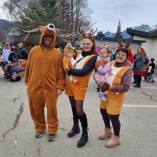 Eine Familie in Rentierkostümen, lächelnd, mit zwei Kindern im Arm, und einem verschneiten Berg im Hintergrund.