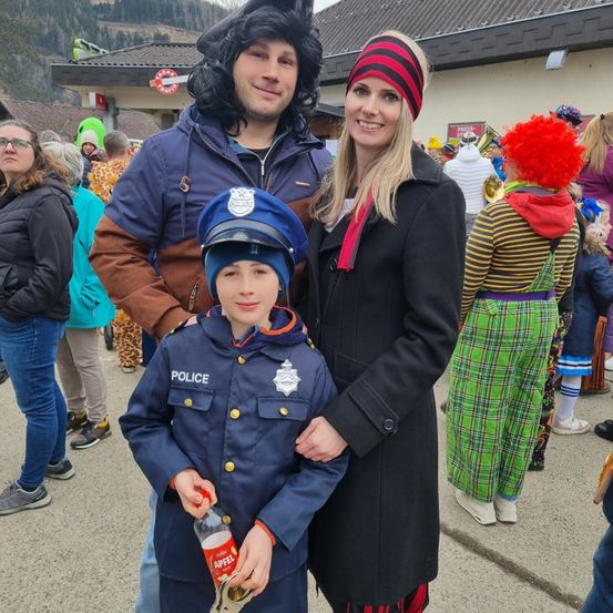 Eine Familie in Kostümen, mit einem Mann in einer Polizeiuniform und einer Frau in einem schwarzen Mantel, posiert für ein Foto bei einer Outdoor-Veranstaltung.