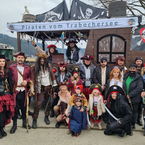 Eine Gruppe von Piraten vom Trabochersee posiert für ein Foto mit ihrem Schiff im Hintergrund. Sie sind alle in Piratenkostümen gekleidet.
