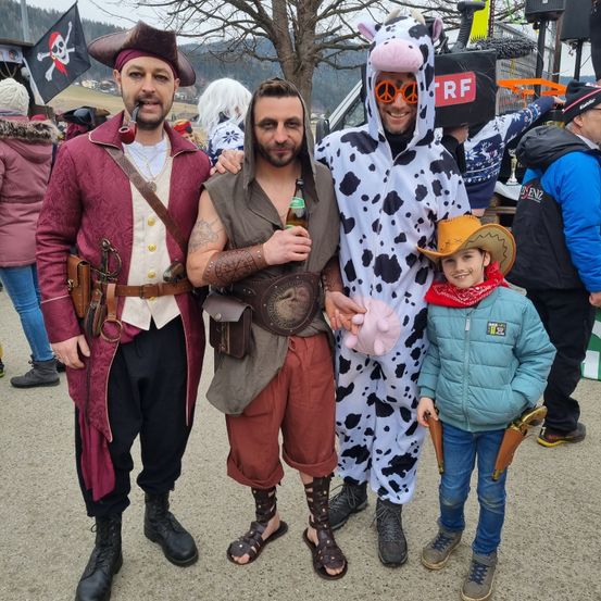 Drei Menschen in Kostümen posieren für ein Foto. Ein Mann in einem Piratenkostüm, ein Mann in einem braunen Umhang und ein Kind in einem Cowboykostüm. Sie stehen vor einem Baum.