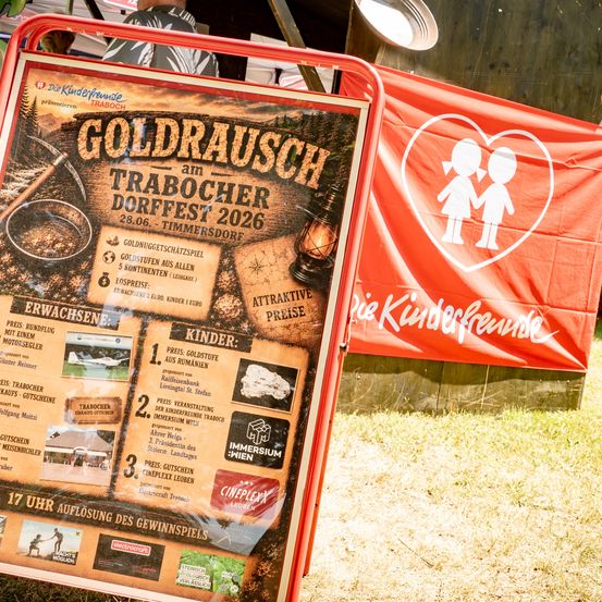 Ein Plakat bewirbt das Goldrausch am Traboscher Dorffest 2026 mit einem Banner von zwei Kindern. Es enthält Details zu Preisen, einschließlich Goldnuggets, Event-Tickets und einem komplexen Leben.