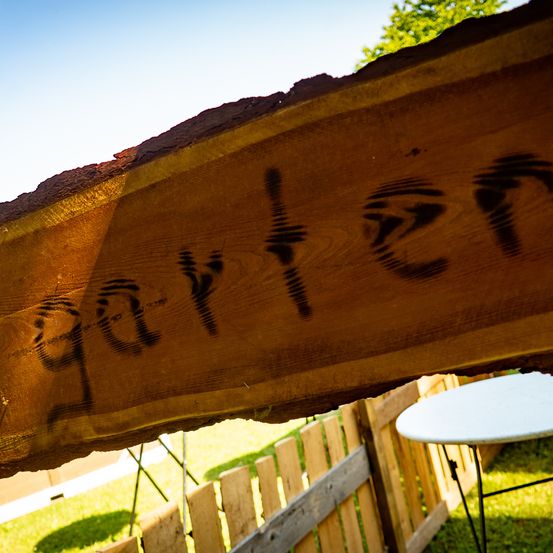 Ein Holzschild mit dem Wort 'Garten' darauf ist über einem Zaun platziert. Das Schild ist aus einem Baumstamm gemacht.