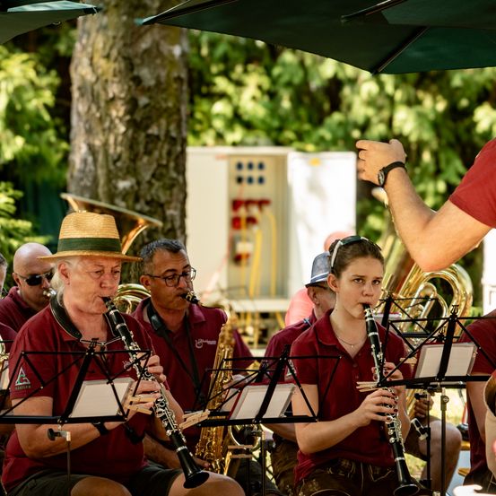 Eine Gruppe von Musikern spielt im Freien. Sie spielen verschiedene Instrumente, darunter Klarinette und Saxophon. Sie sind alle in roten Hemden gekleidet.