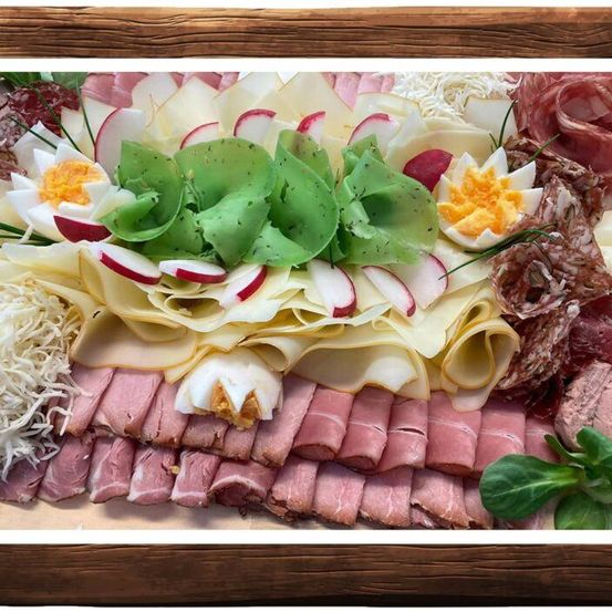 Ein Charcuterie-Brett mit verschiedenen Fleischsorten, Käse und Gemüse, darunter Schinken, Käsescheiben, Radieschen und grüne Blätter. Dekoriert mit einer blumenartigen Gestaltung aus Eiern und Käse.