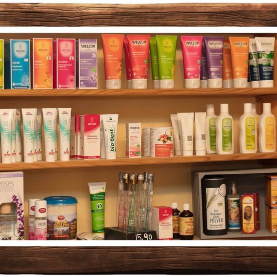 Ein Holzregal zeigt verschiedene Weleda-Hautpflegeprodukte, darunter Lotionen, Shampoos und Conditioner, zusammen mit anderen Schönheitsartikeln. Das Regal ist ordentlich organisiert, mit ordentlich gestapelten Produkten.