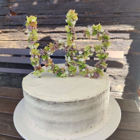 Ein weißer Kuchen mit einer dekorativen Blumendekoration oben, die die Zahl 60 bildet, steht auf einem weißen Teller auf einem Holztisch.