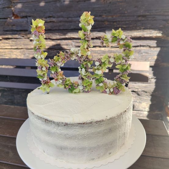 Ein weißer Kuchen mit einer dekorativen Blumendekoration oben, die die Zahl 60 bildet, steht auf einem weißen Teller auf einem Holztisch.