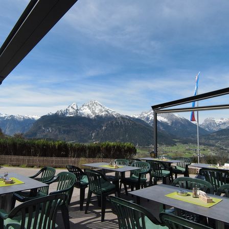 Outdoor dining area with a view of snowy mountains. Tables and chairs are set up, and a flag is visible on the right.