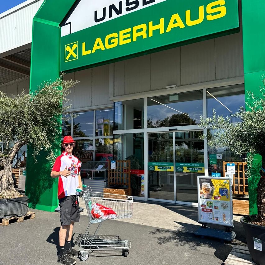 A man in a red and white shirt with a red hat pushes a shopping cart in front of a green Lagerhaus store.