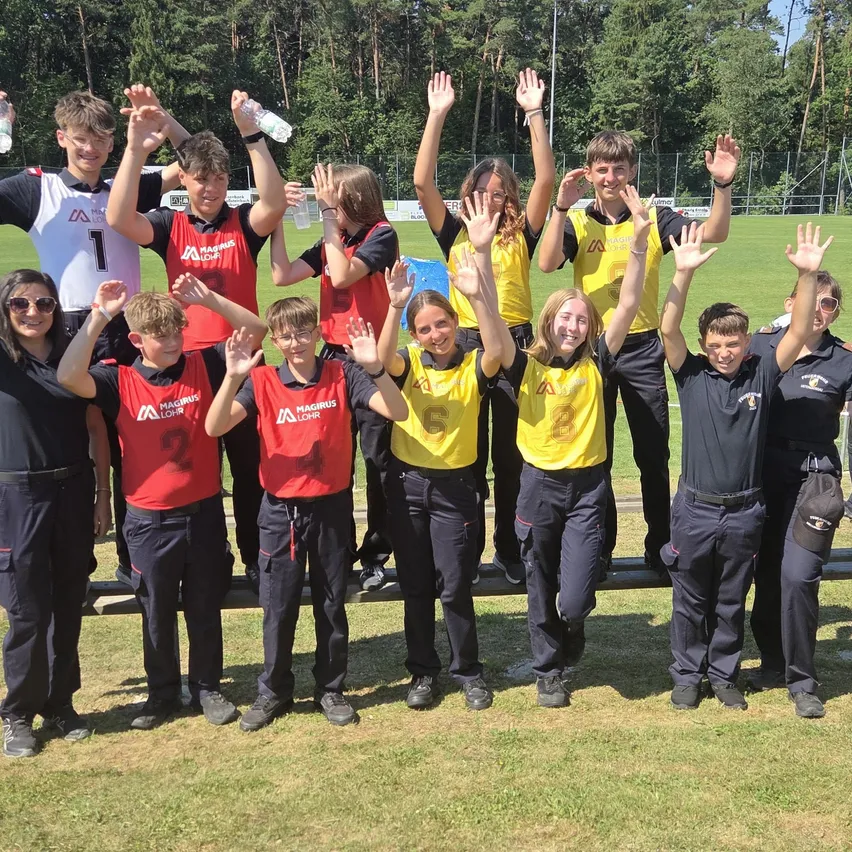 Eine Gruppe junger Leute in Sporttrikots posiert für ein Foto auf einem Feld. Sie halten Wasserflaschen in der Hand und lächeln.