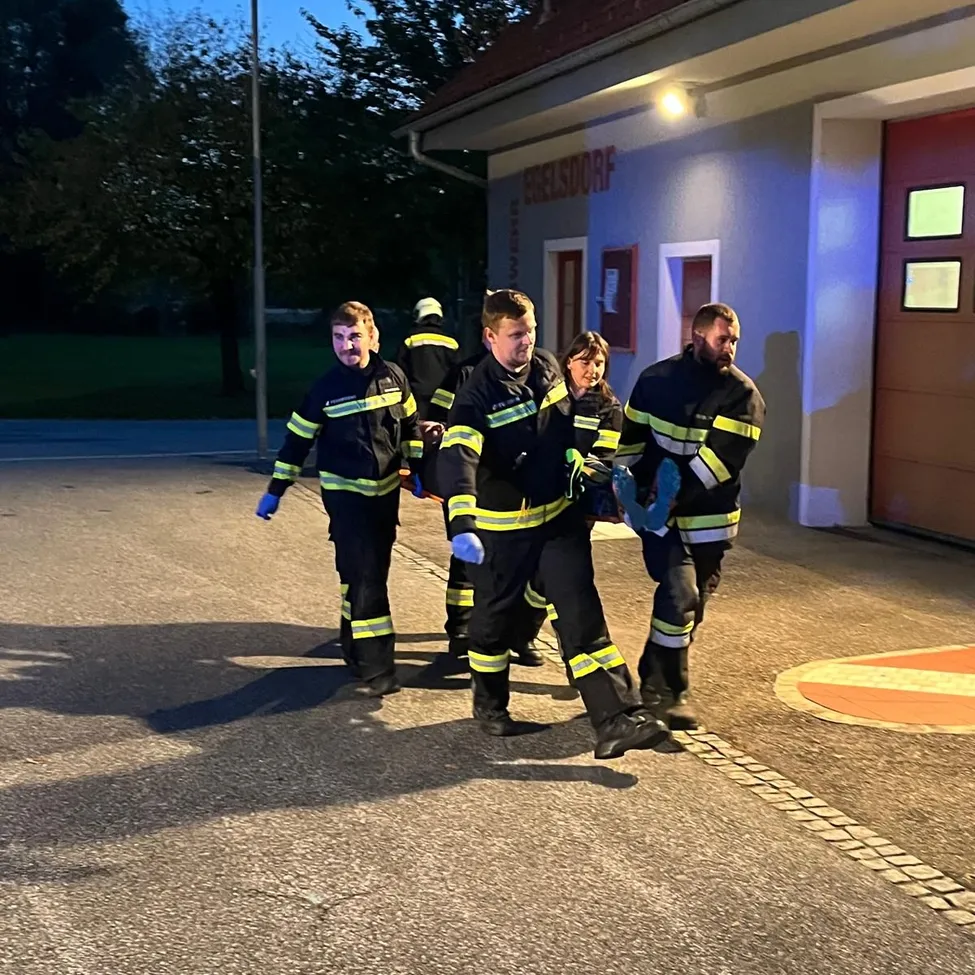 Eine Gruppe von Feuerwehrleuten geht nachts vor einem Feuerwehrhaus.