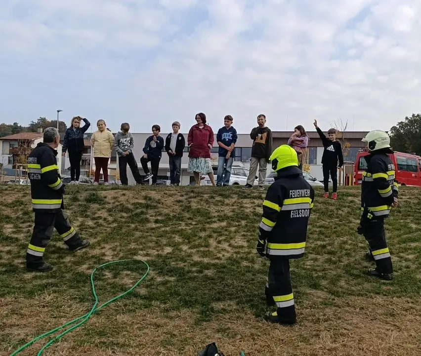 Eine Gruppe von Feuerwehrleuten demonstriert eine Brandschutzübung auf einem Grashügel.
